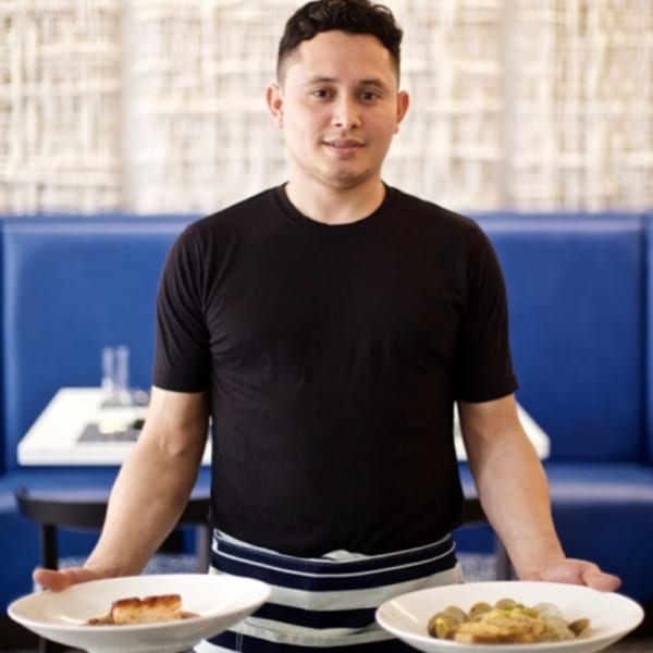 All Set Restaurant & Bar server holding two plates of seafood dishes in a blue booth setting.
