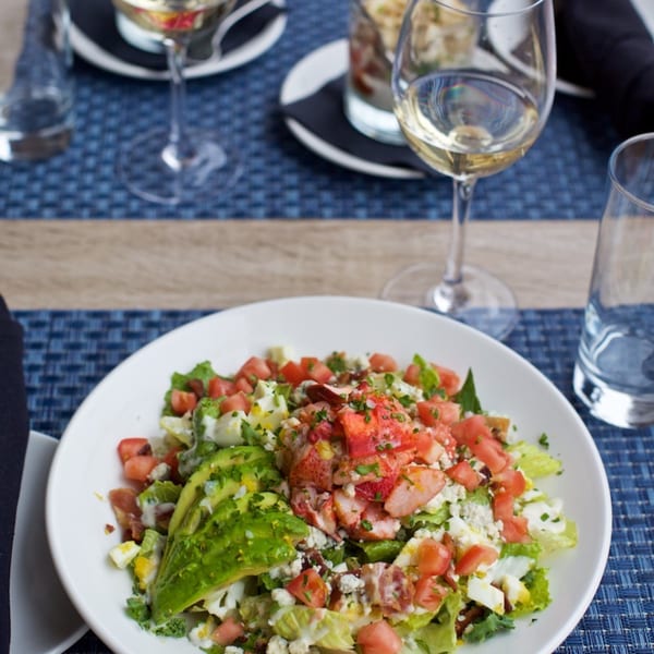 All Set Restaurant & Bar's lobster cobb salad with avocado, tomatoes, and blue cheese, with wine glasses.