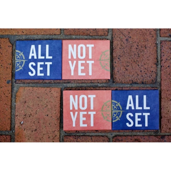Two pairs of blue and coral signs on a brick surface, reading "ALL SET" and "NOT YET".