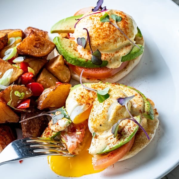 All Set Restaurant & Bar's Eggs Benedict with avocado, tomato, and a side of crispy potatoes.