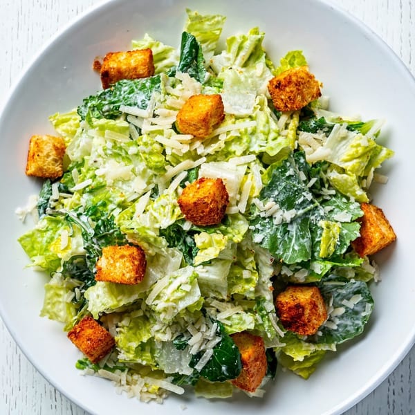 Overhead view of a Caesar salad with romaine lettuce, croutons, and shredded Parmesan cheese.