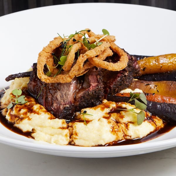 Braised short rib with mashed potatoes, roasted carrots, crispy onion rings, and gravy.