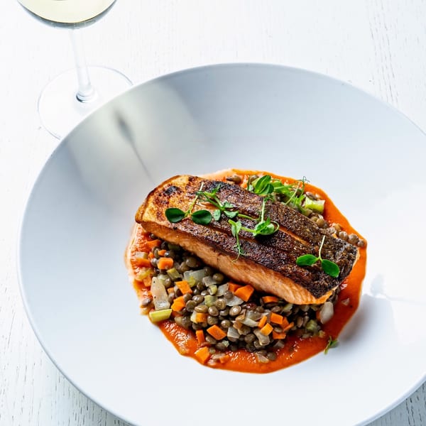 Pan-seared salmon with crispy skin, served over lentils and diced vegetables in a red sauce.