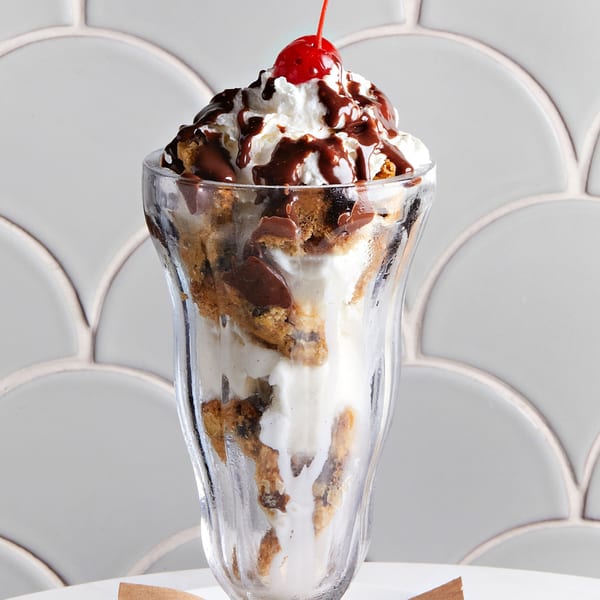 A tall glass of ice cream with cookie pieces, chocolate syrup, whipped cream, and a cherry.