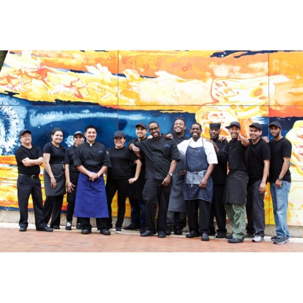 The All Set Restaurant & Bar team, a diverse group of staff and chefs, smiling in front of a vibrant mural.