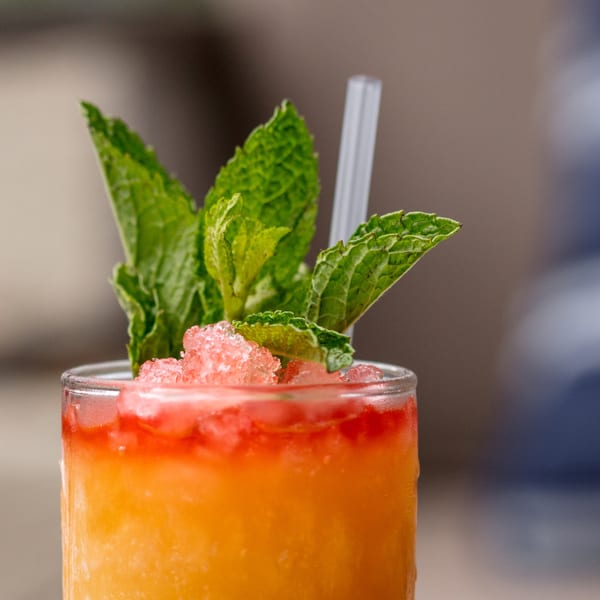 Close-up of a vibrant orange and red cocktail with crushed ice, mint sprigs, and a straw.