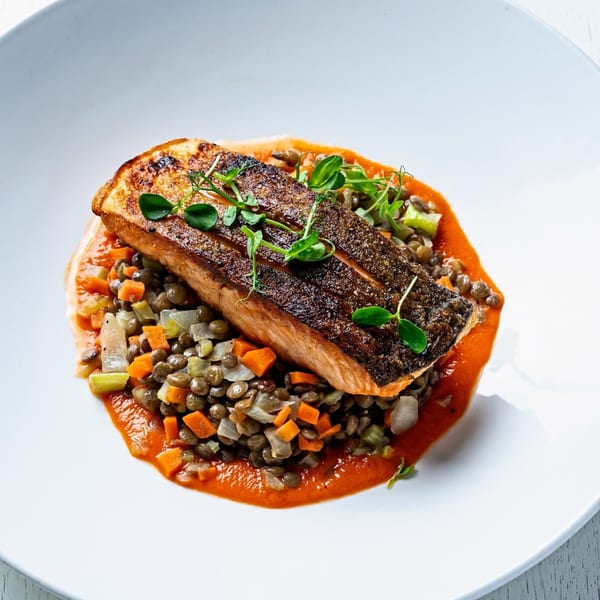 Pan-seared salmon with crispy skin, served over lentils, diced vegetables, and a red sauce.