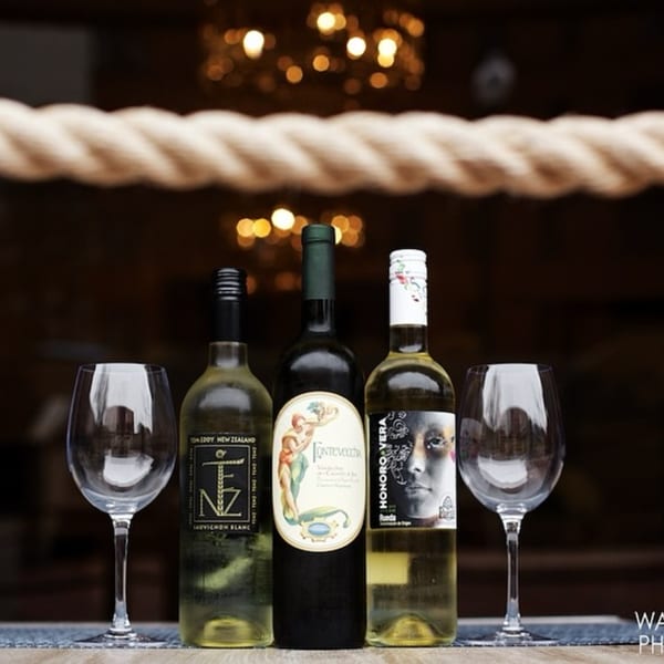 Three bottles of white wine and two empty wine glasses on a table with a rope decoration.