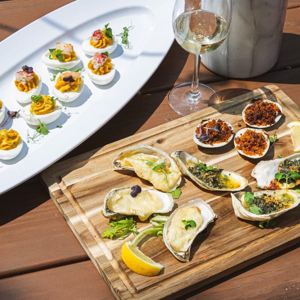 Deviled eggs, baked oysters, and clams with breadcrumbs on a wooden board with white wine.