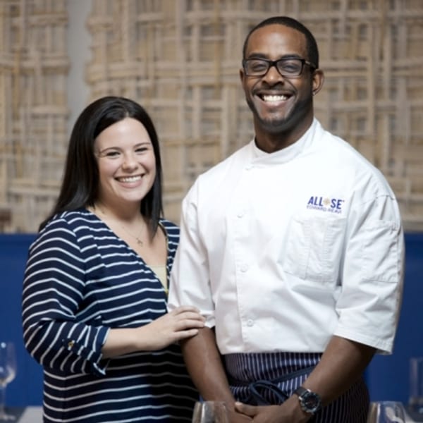 A smiling woman in a striped shirt and a smiling chef in a white uniform with the All Set logo.