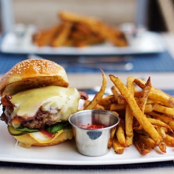 A cheeseburger with melted cheese, pickles, and lettuce, served with a side of fries and ketchup.