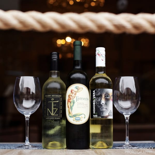 Three bottles of white wine and two empty wine glasses on a table with a blurred background.