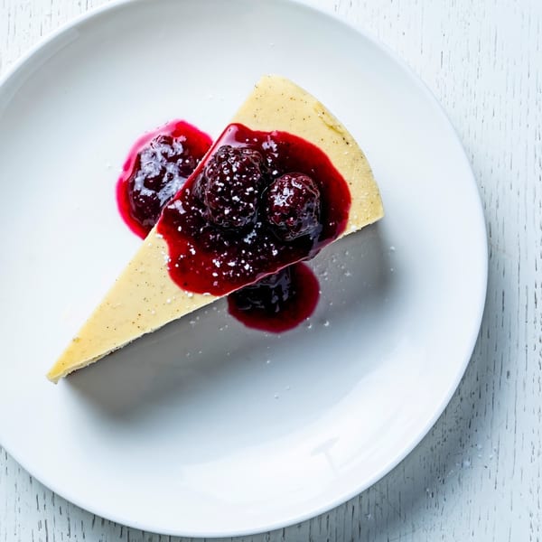 A slice of cheesecake with berry compote and powdered sugar on a white plate.