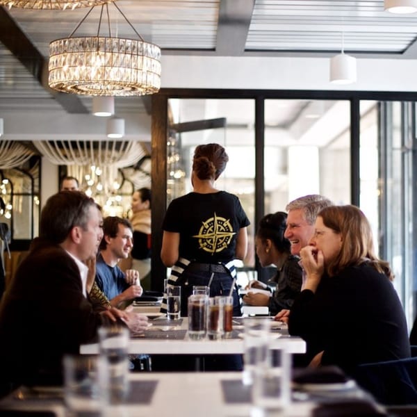 Diners seated at tables in All Set Restaurant & Bar, with a server in a compass-logo shirt.