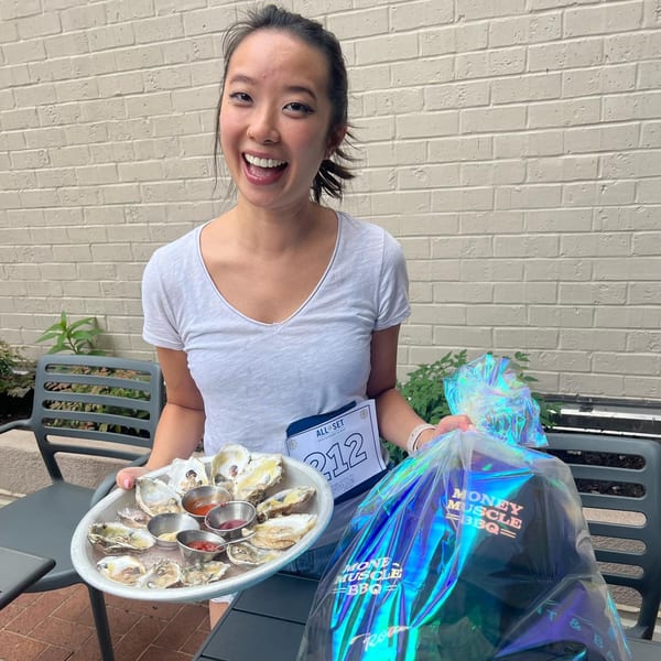 A smiling woman holds a tray of oysters and a shiny bag from All Set Restaurant & Bar.