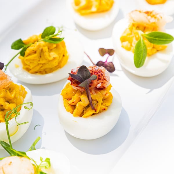Deviled eggs with yellow filling, topped with lobster and microgreens on a white platter.