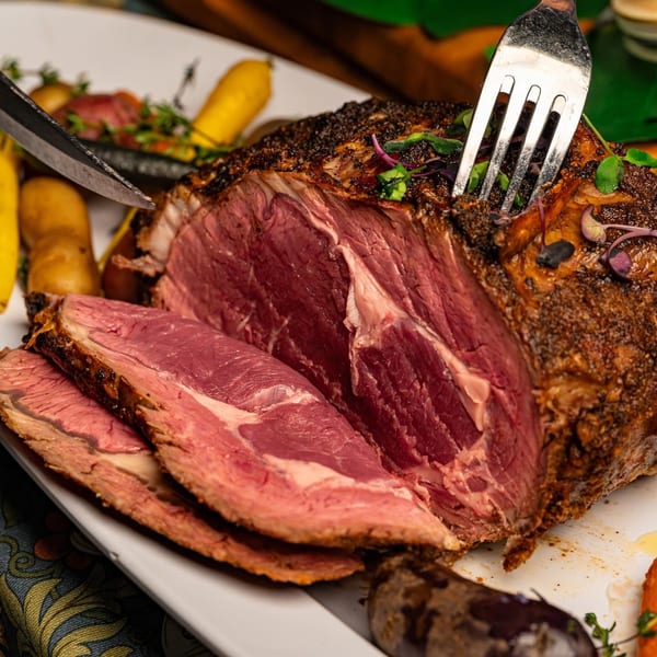 A large, perfectly cooked prime rib roast, partially sliced, with a fork and knife ready to serve.
