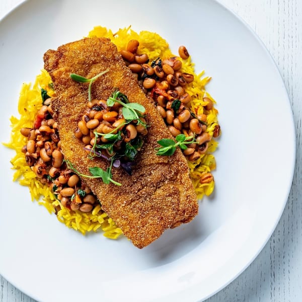 Crispy fried fish fillet on a bed of yellow rice and black-eyed peas, garnished with microgreens.