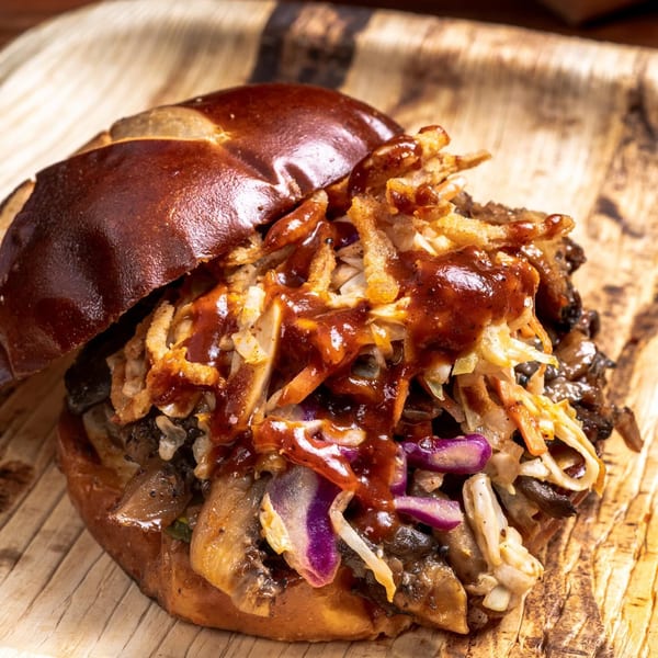 Close-up of a BBQ pulled pork sandwich on a pretzel bun with coleslaw and crispy onions.