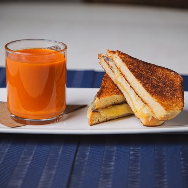 Grilled cheese sandwich with melted cheese and a glass of tomato soup on a white plate.