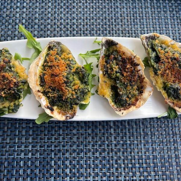 Four baked oysters with green filling and breadcrumbs on a white plate with arugula.