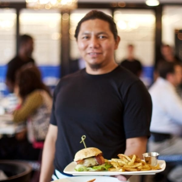 A server at All Set Restaurant & Bar holds a plate with a burger and french fries.