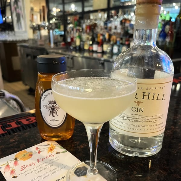 A "Bees Knees" cocktail, honey, and Barr Hill Gin bottle on a bar counter at All Set Restaurant & Bar.