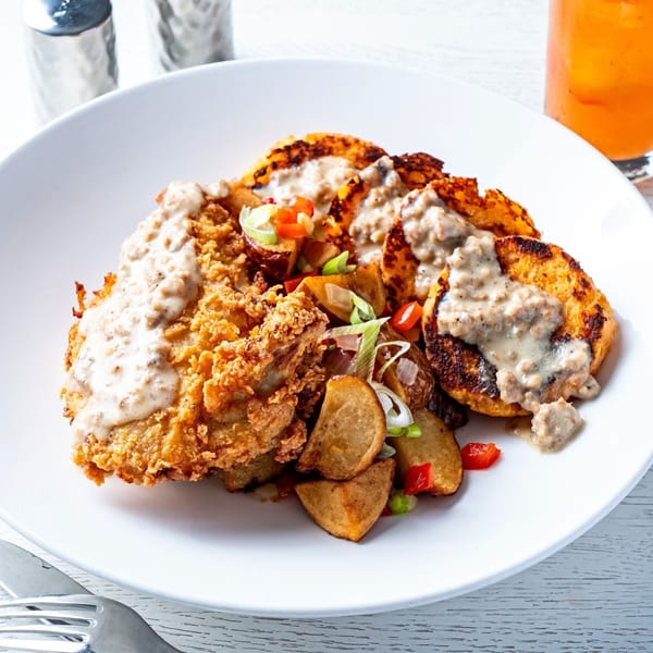 Fried chicken and biscuits with gravy, roasted potatoes, and peppers on a white plate.