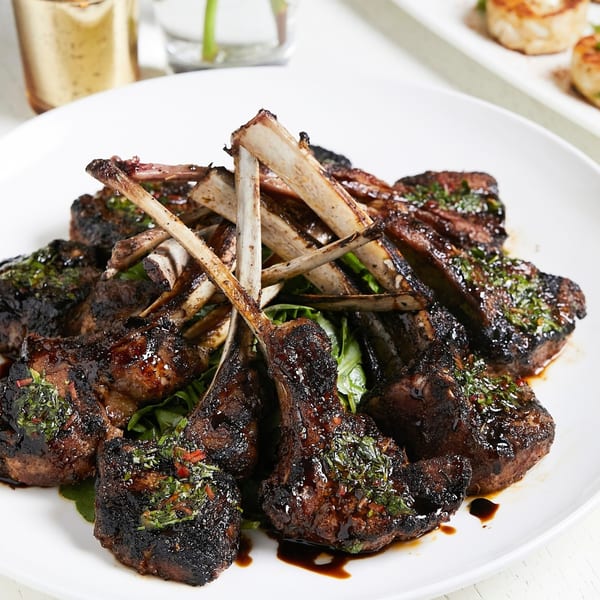 Grilled lamb chops with a dark glaze and fresh herbs, served on a bed of greens.