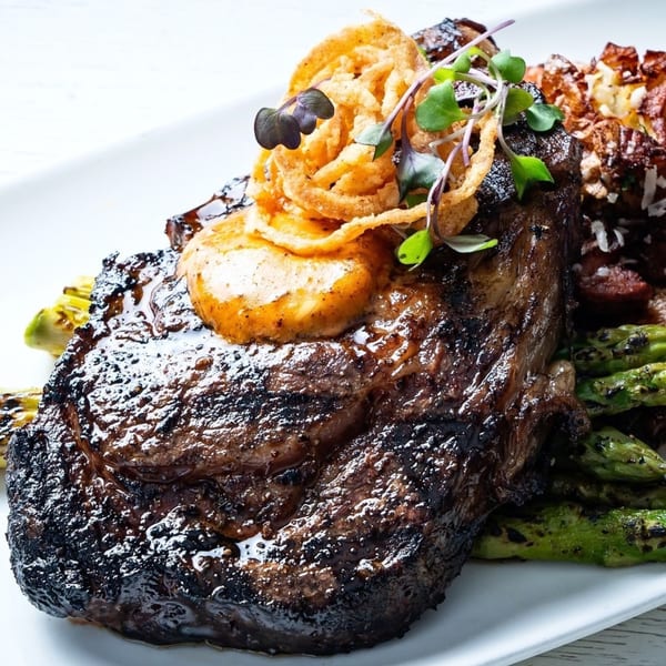 Grilled steak with melted butter, crispy onion rings, microgreens, asparagus, and roasted potatoes.