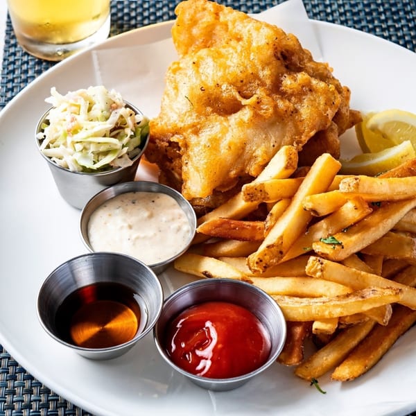 Golden-brown fried fish and french fries with coleslaw, tartar sauce, and ketchup on a white plate.