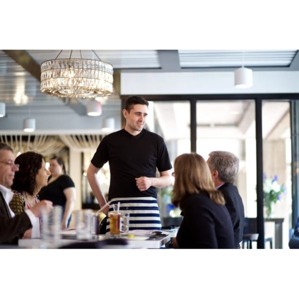 A server in a striped apron talks to customers seated at a table in All Set Restaurant & Bar.