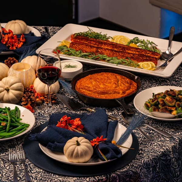 A festive table set with a large salmon fillet, side dishes, wine, and autumn decor.