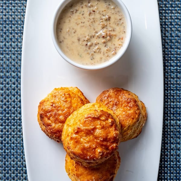 Golden brown biscuits with a side of creamy sausage gravy on a white plate.