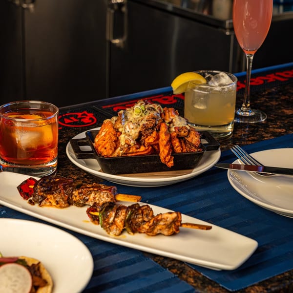 All Set Restaurant & Bar's seafood skewers, loaded fries, and cocktails on a bar.